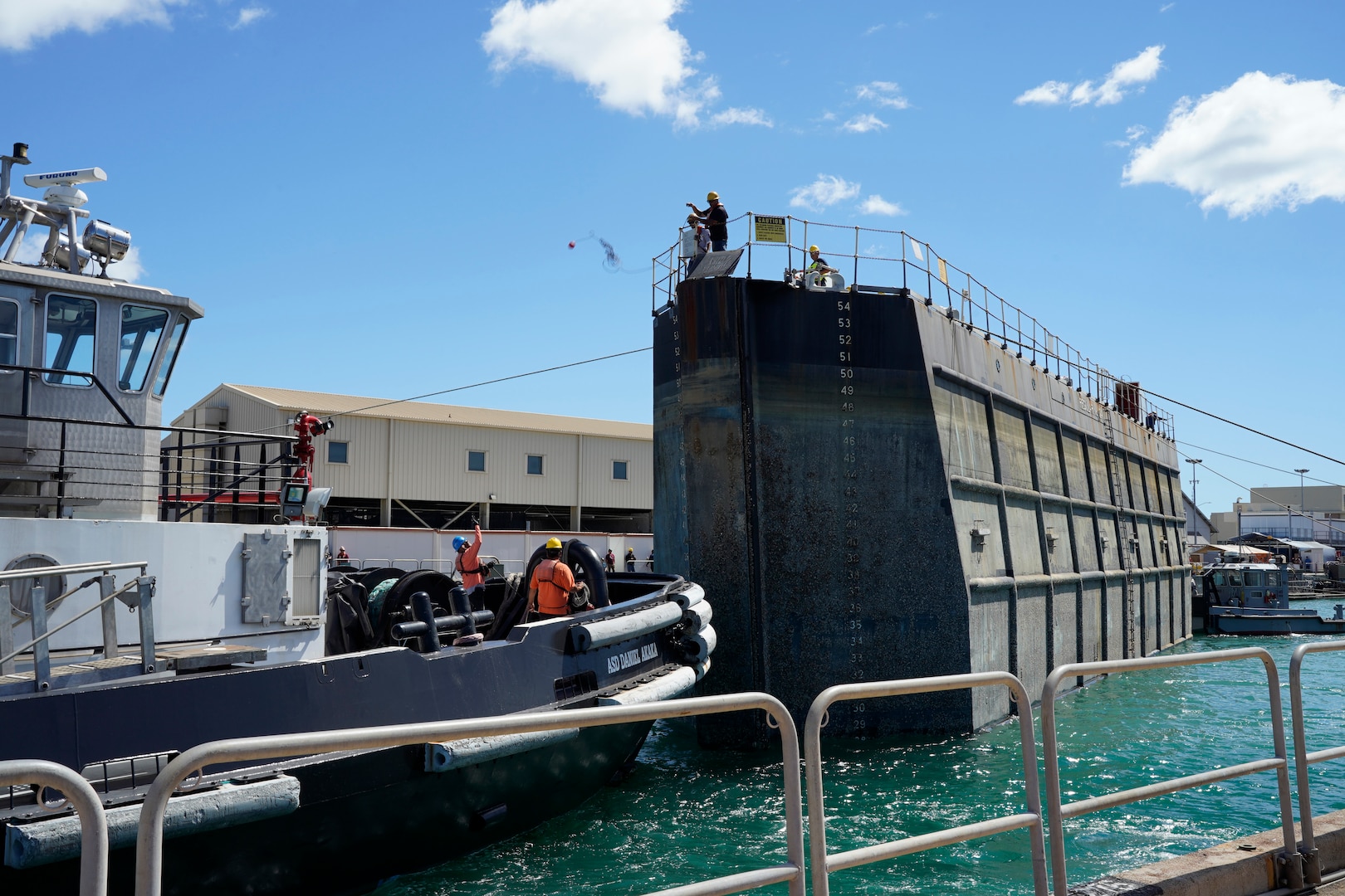 A Pearl Harbor Naval Shipyard & Intermediate Maintenance Facility worker tosses a line from the caisson to personnel on tugboat ASD Daniel Akaka during the undocking of the Virginia-class attack submarine USS Minnesota (SSN 783) from Dry Dock 2, Oct. 12, 2023.