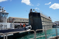 A Pearl Harbor Naval Shipyard & Intermediate Maintenance Facility worker tosses a line from the caisson to personnel on tugboat ASD Daniel Akaka during the undocking of the Virginia-class attack submarine USS Minnesota (SSN 783) from Dry Dock 2, Oct. 12, 2023.