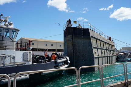 A Pearl Harbor Naval Shipyard & Intermediate Maintenance Facility worker tosses a line from the caisson to personnel on tugboat ASD Daniel Akaka during the undocking of the Virginia-class attack submarine USS Minnesota (SSN 783) from Dry Dock 2, Oct. 12, 2023.