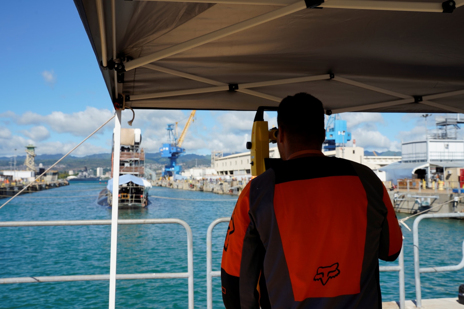 A Pearl Harbor Naval Shipyard & Intermediate Maintenance Facility employee uses an instrument to direct line handlers during the undocking of the Virginia-class attack submarine USS Minnesota (SSN 783) from Dry Dock 2, Oct. 12, 2023.