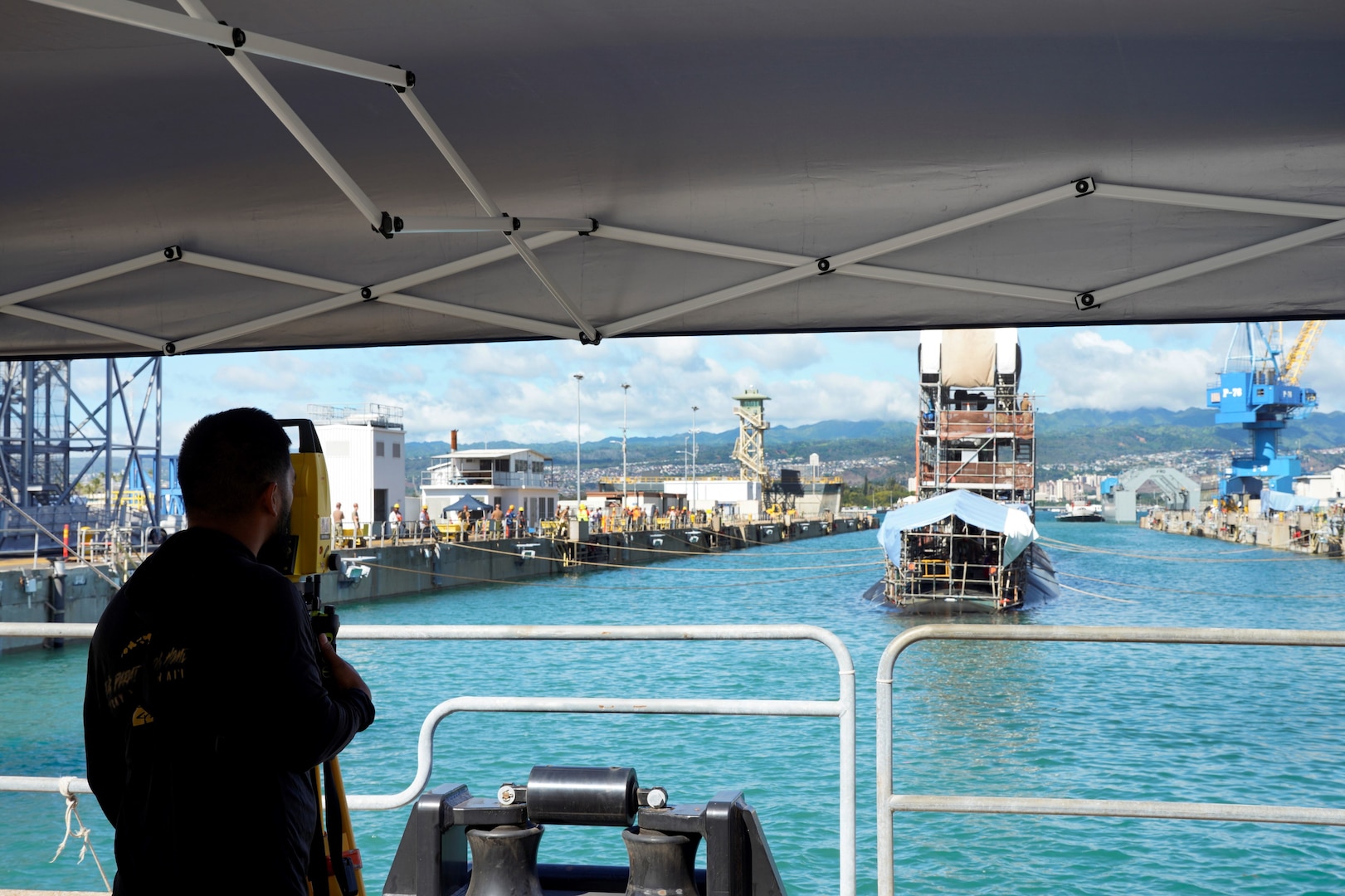 A Pearl Harbor Naval Shipyard & Intermediate Maintenance Facility employee uses an instrument to direct line handlers during the undocking of the Virginia-class attack submarine USS Minnesota (SSN 783) from Dry Dock 2, Oct. 12, 2023.