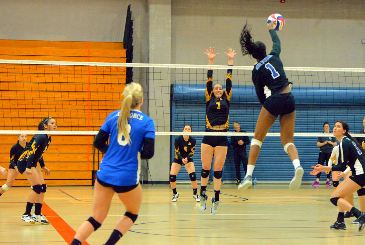 Air Force athlete returns a volleyball across the net with the opposing squad poised to block its return.