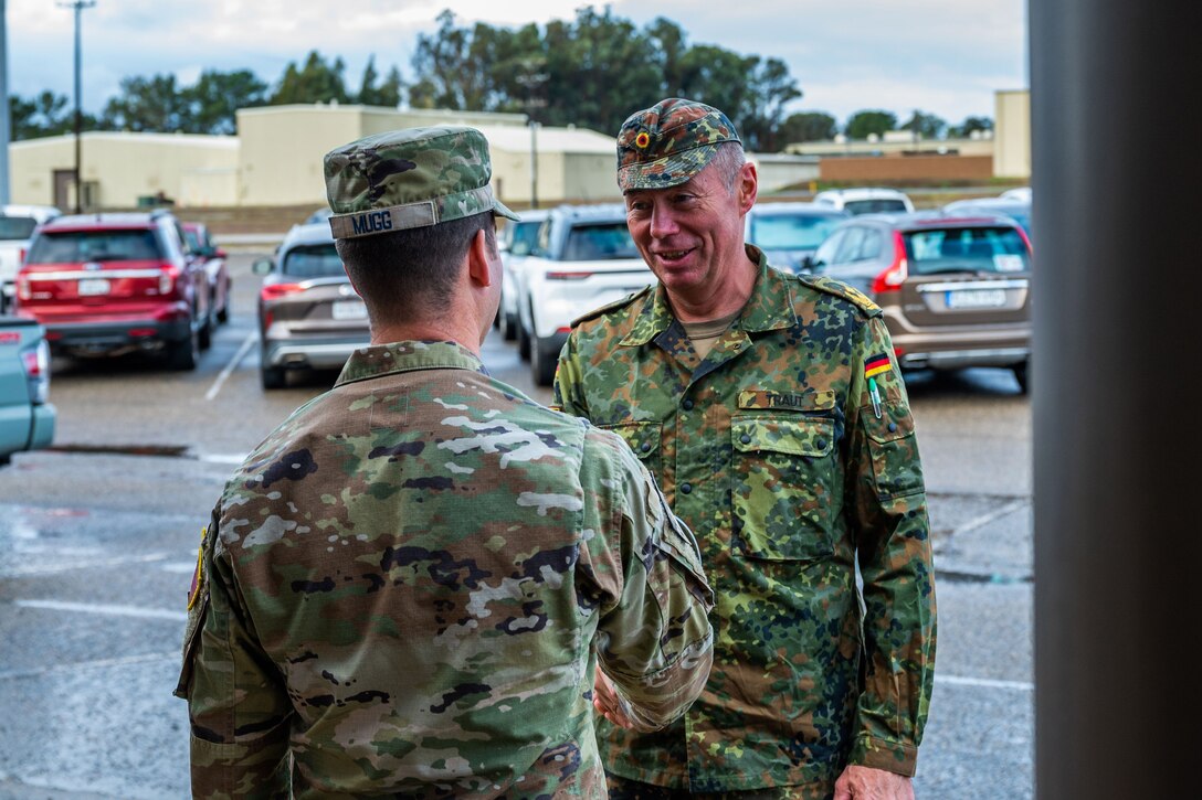 Two men in military uniforms speak to each other outside a building.