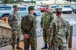 Four men in military uniforms speak to each other outside a building.