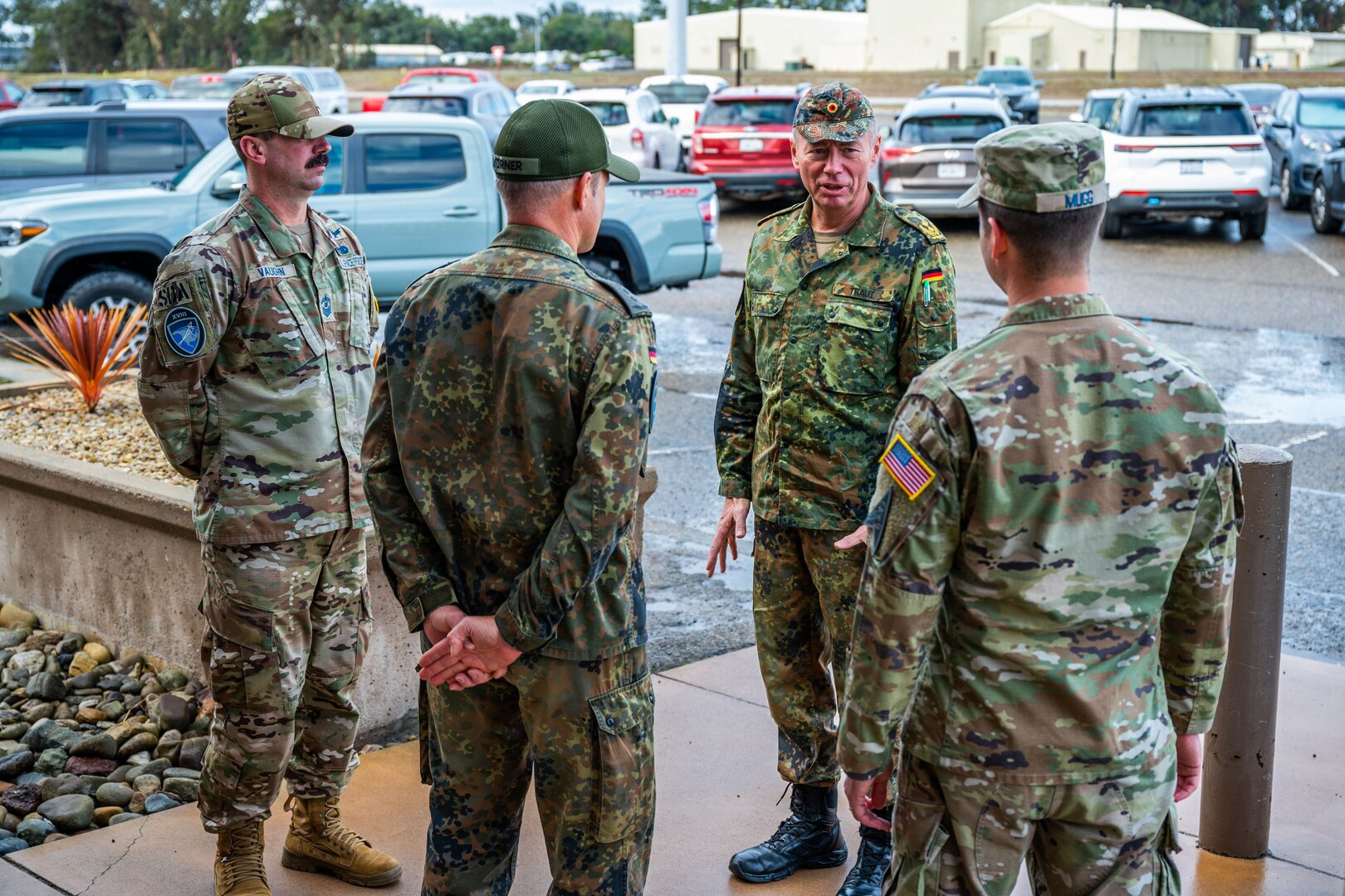 Four men in military uniforms speak to each other outside a building.