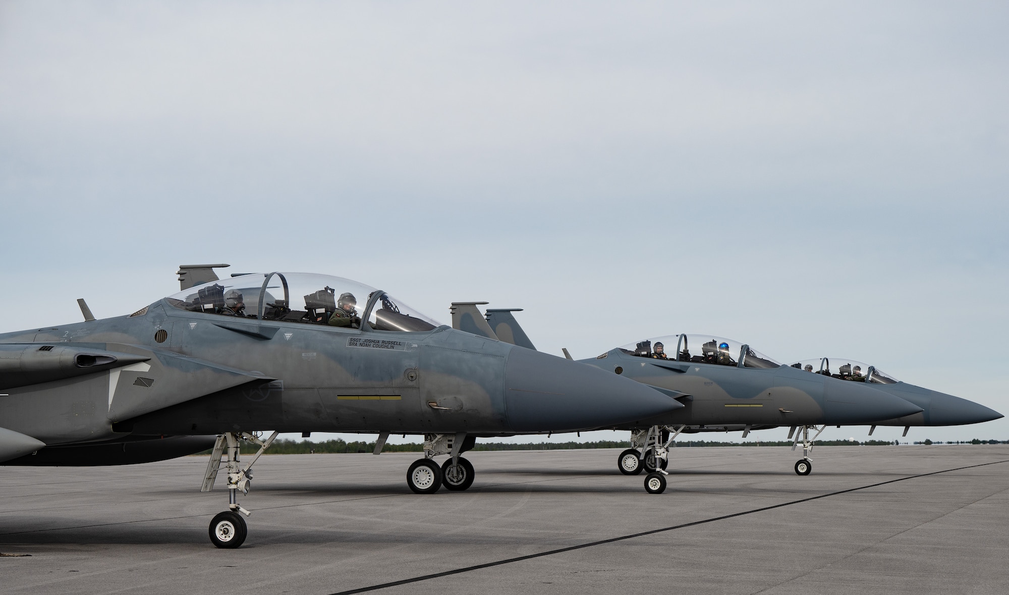 Staggered fighter jets rest on the flight line.