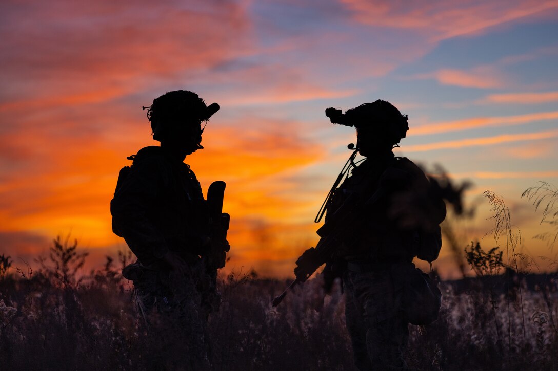 Two Marines are seen in silhouette against an orange sky.