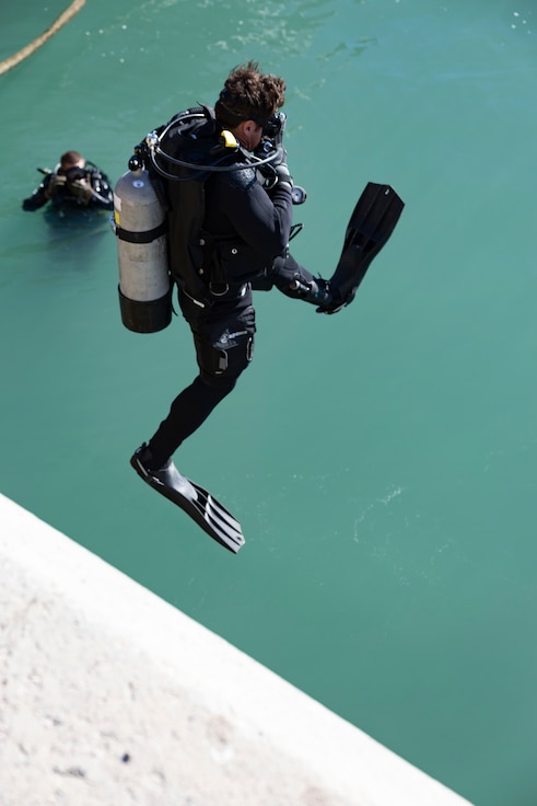 Steelworker 2nd Class Cooper Rekstis, assigned to Underwater Construction Team 1 (UCT 1), enters the water to perform an underwater inspection of an overturned barge in Rota, Spain, Nov. 14, 2023.
