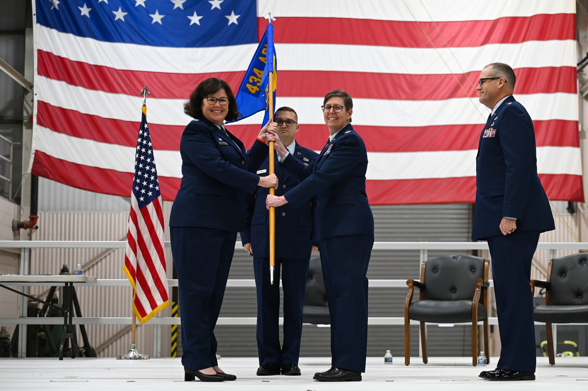 Two women, both in current Air Force service dress uniforms, pose with a guidon. Two men, one directly behind the women and one to the photographer's right of the women, stand "at attention" to witness the event (a change of command ceremony).