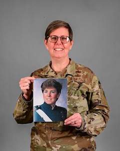A woman, Gretchen Wiltse, poses in a current Air Force OCP uniform with a photo of herself from the late 1980s in an Air Force service uniform from her days at the U.S. Air Force Academy.
