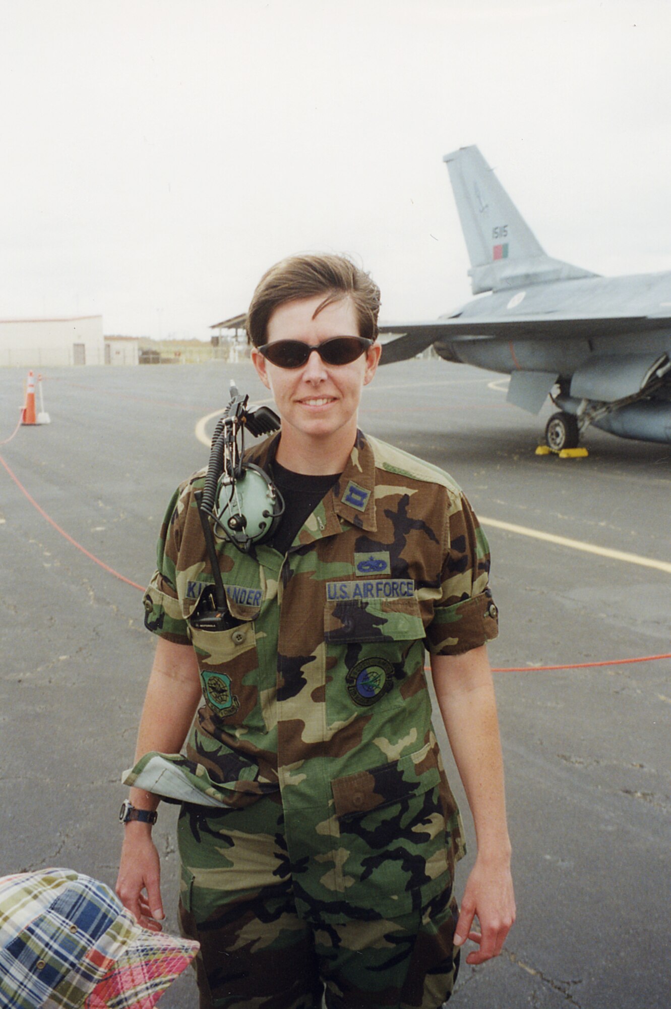 A woman in an old Air Force uniform, with captain rank insignia, poses for a photo in front of a jet.