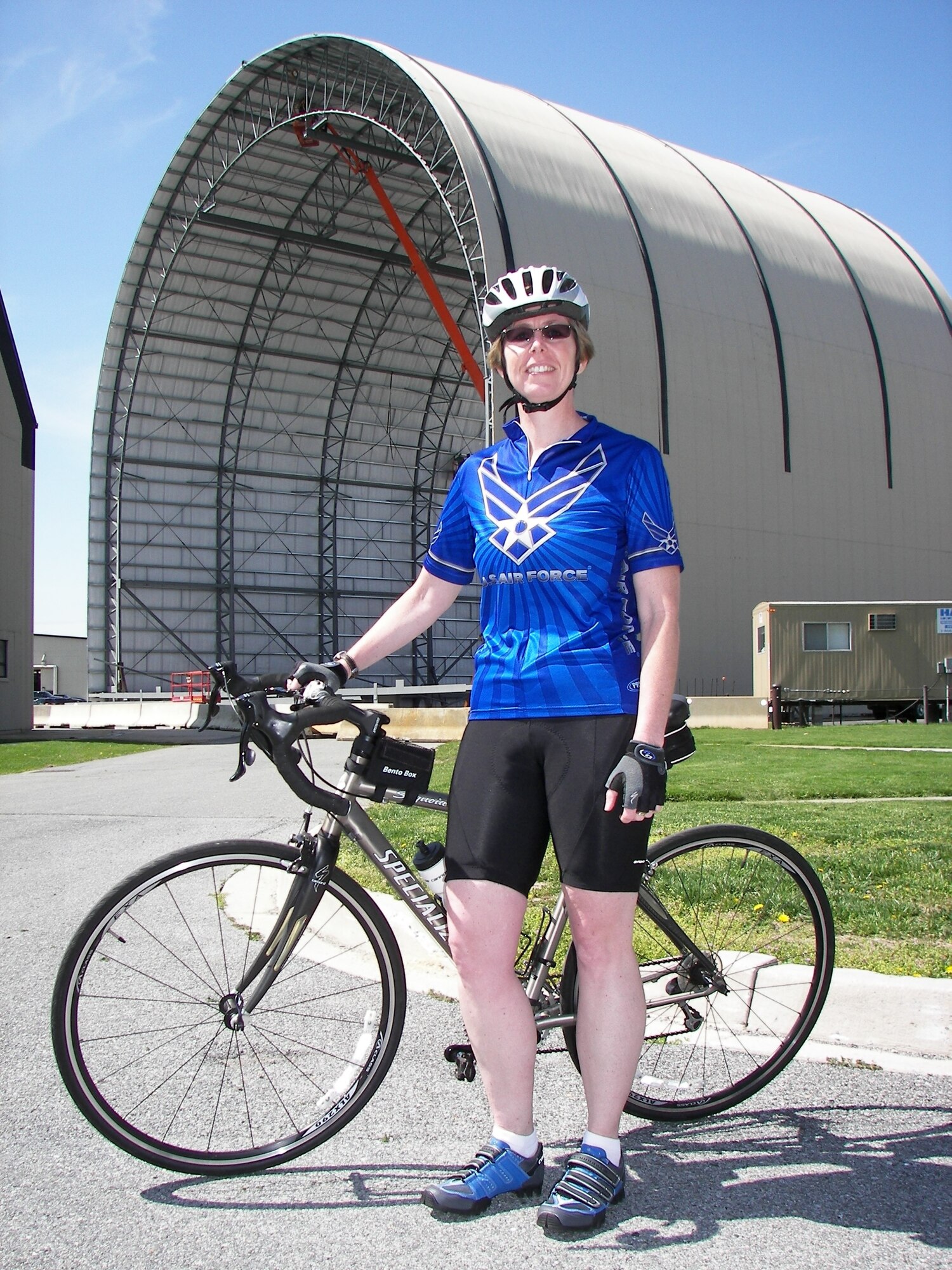 Gretchen Wiltse, with a helmet and blue Air Force biking jersey on, poses with a bicycle.