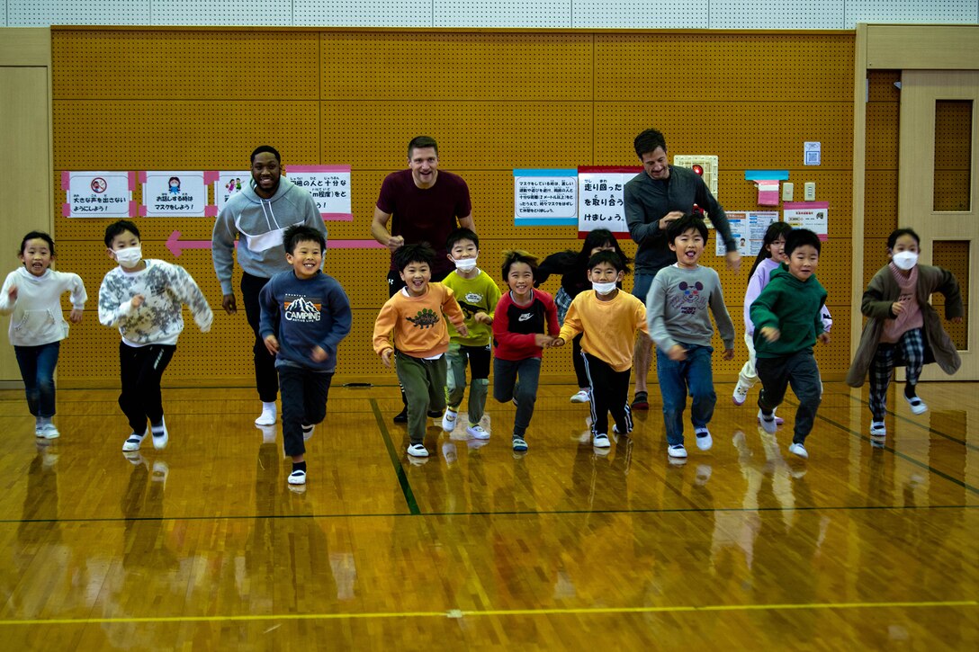 Service members and children run in a community center gym.