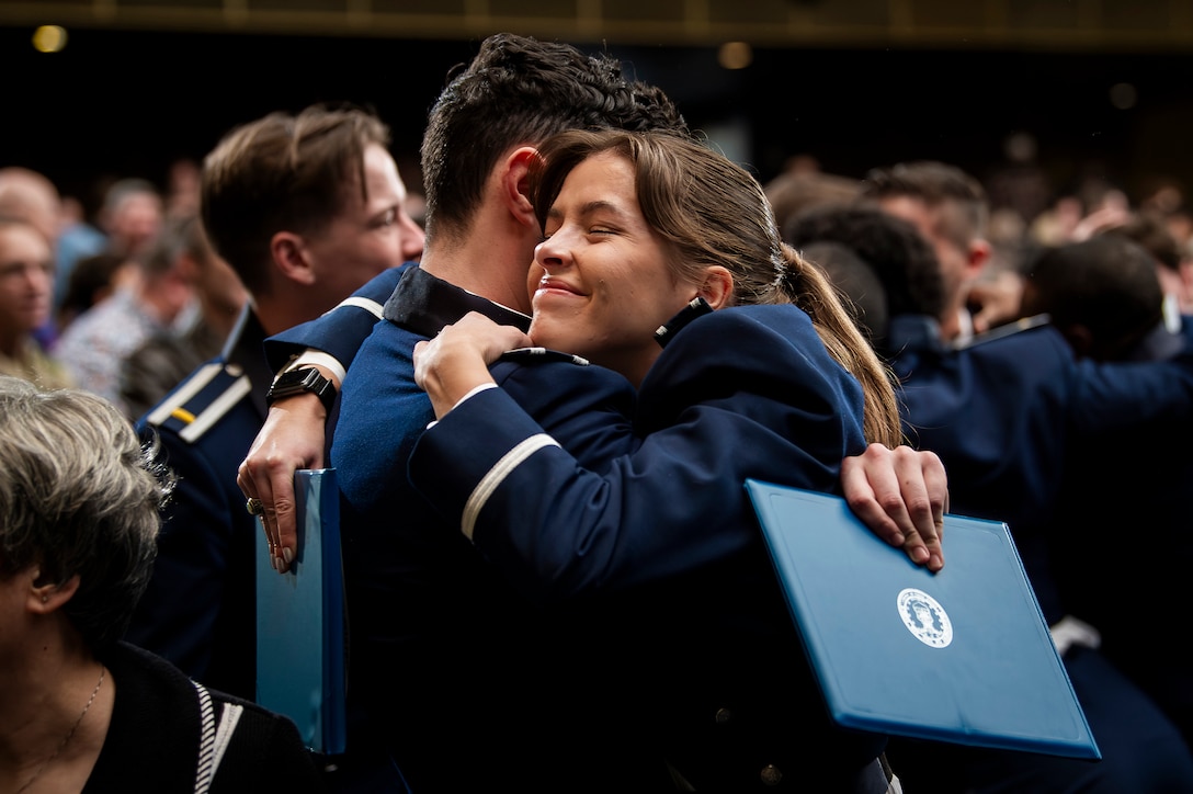 Air Force academy graduates embrace at a graduation ceremony.