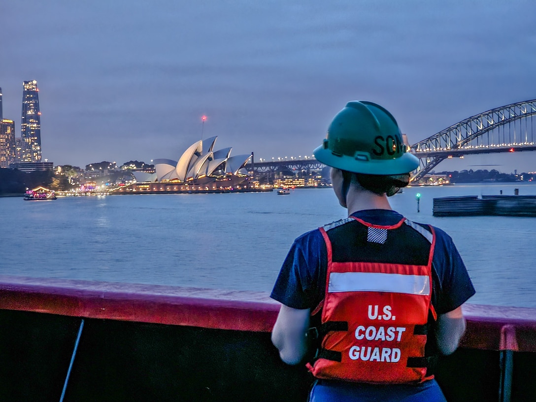 U.S. Coast Guard Seaman Apprentice Mary Wysong looks at the Sydney Opera House while standing on the bow of the U.S. Coast Guard Cutter Polar Star (WAGB 10) as it pulls into Sydney, Australia, Dec. 10, 2023. U.S. Coast Guard Cutter Polar Star is en route to Antarctica in support of Operation Deep Freeze, a joint service, inter-agency support operation for the National Science Foundation, which manages the United States Antarctic Program. (U.S. Coast Guard photo by Petty Officer 3rd Class Ryan Graves)