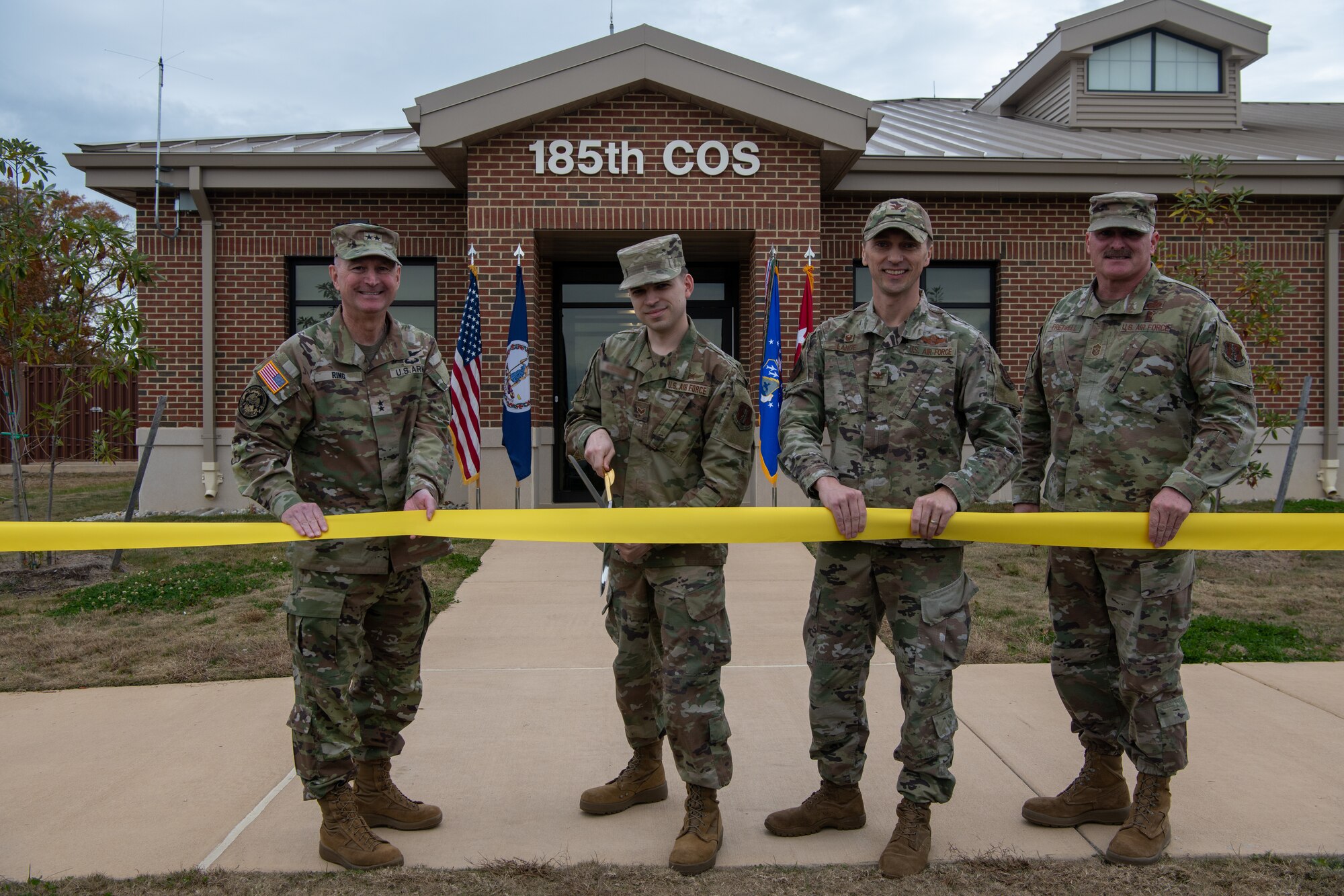 Four military members holding ribbon, one cutting with scissors.