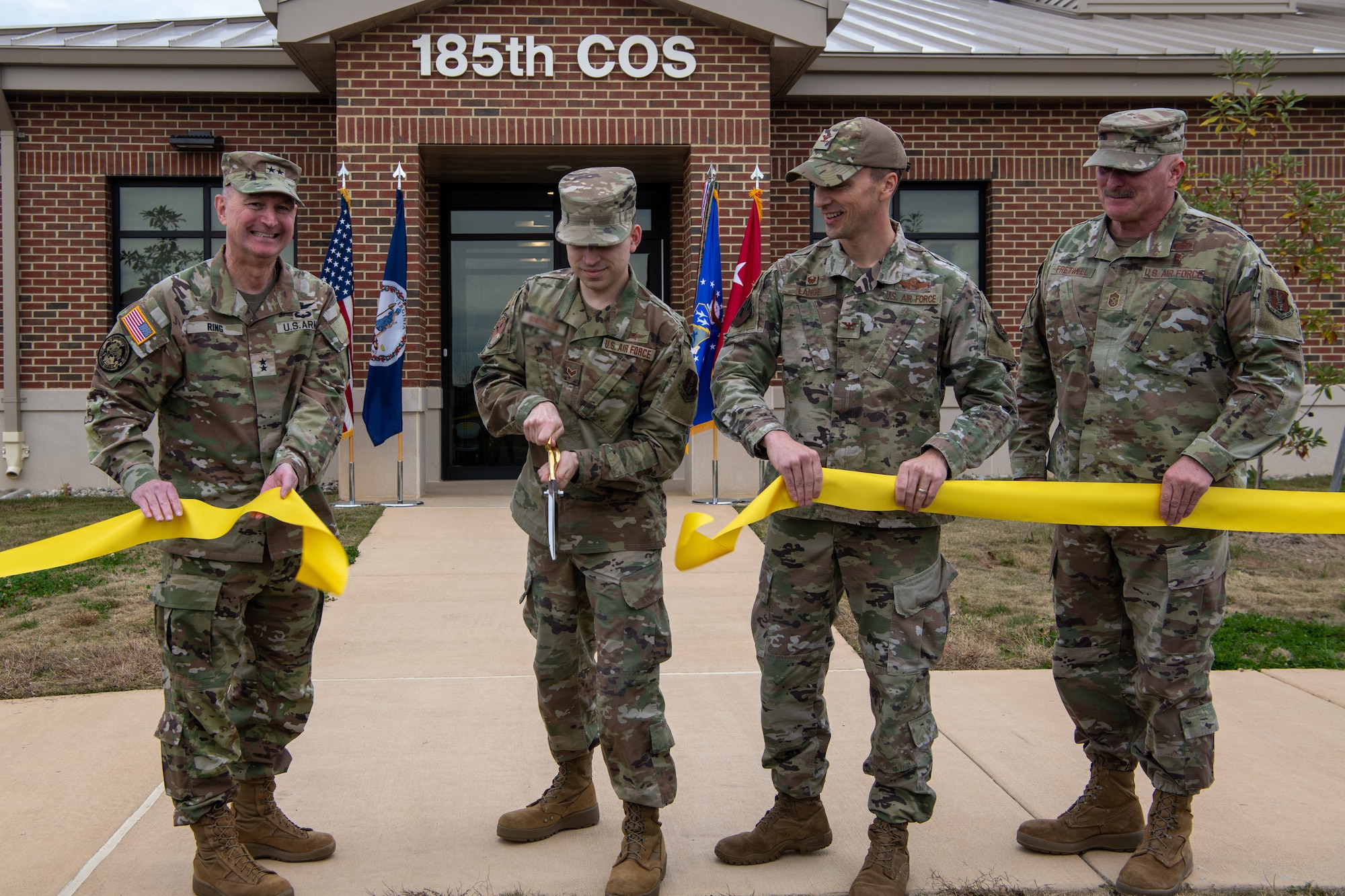 Four military members holding yellow ribbon, one cutting with scissors.
