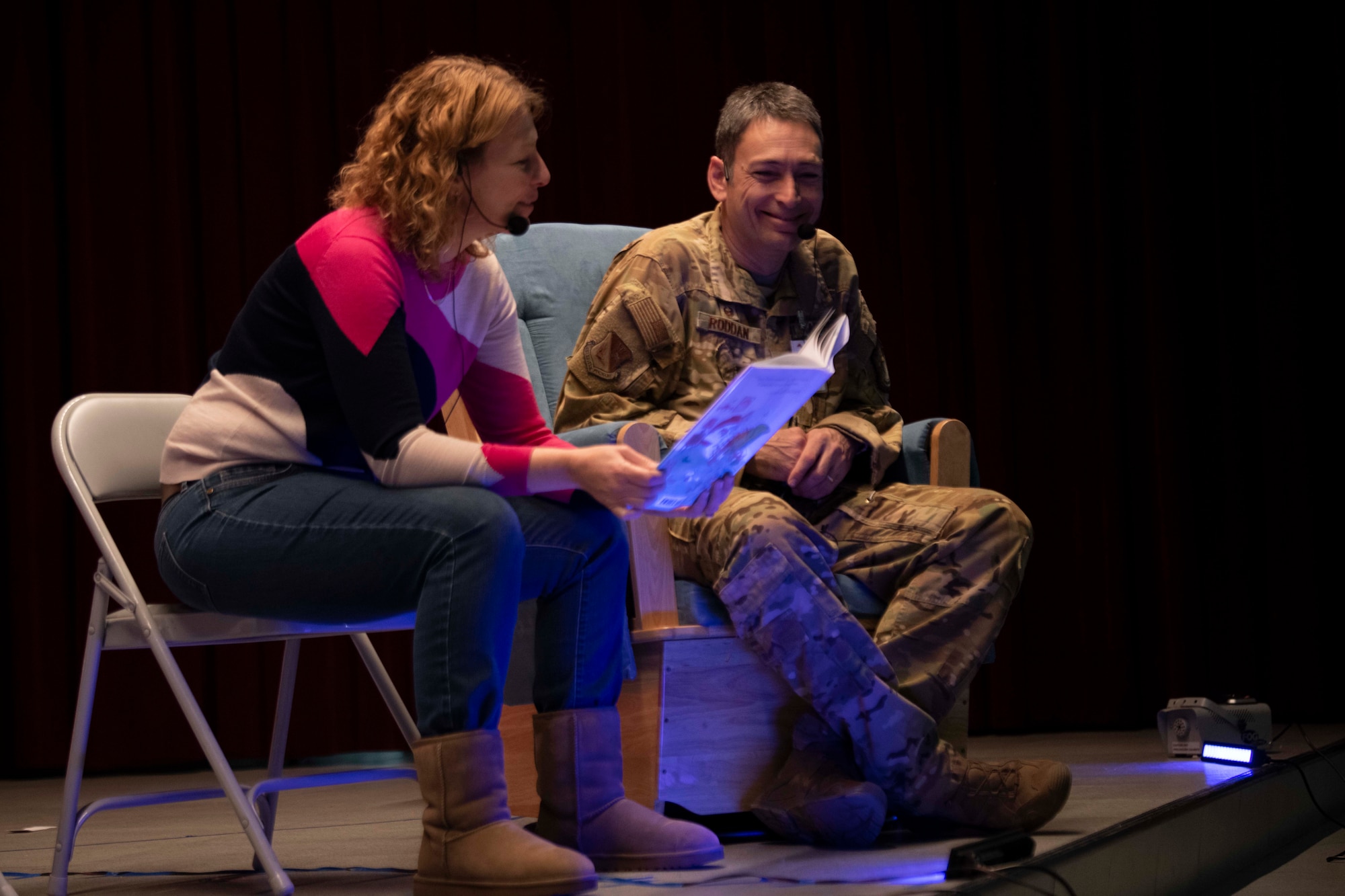 A military man and a woman read a book on stage.