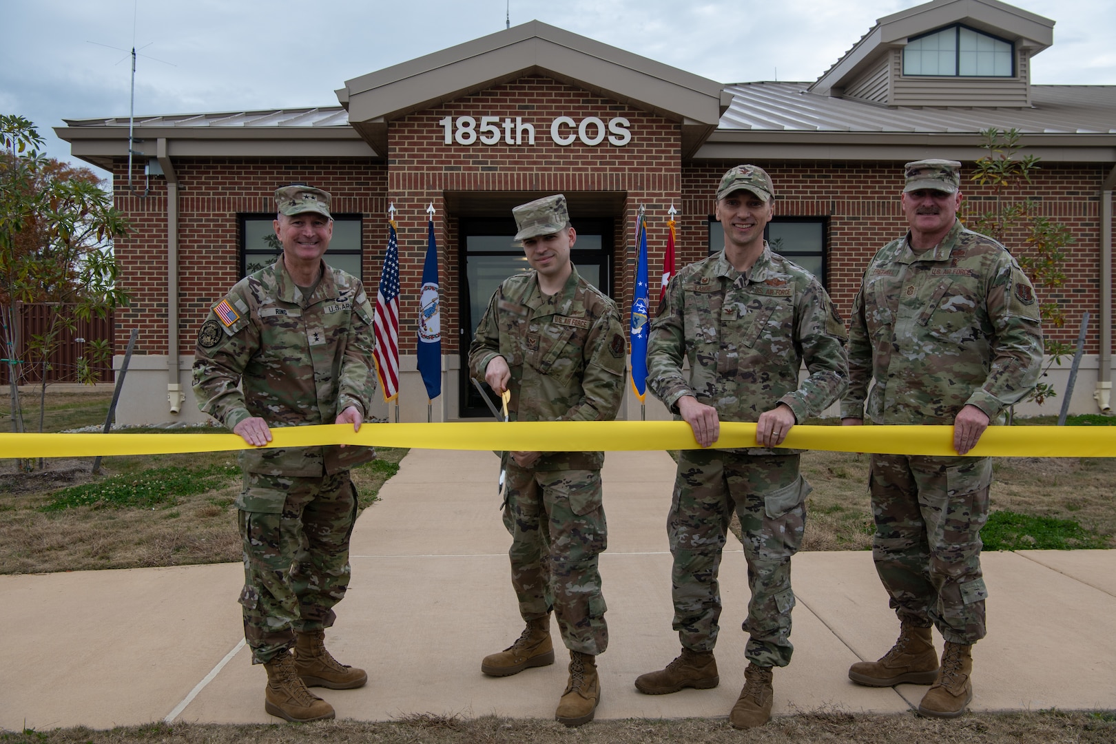 Four military members holding ribbon, one cutting with scissors.