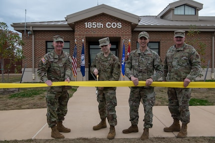 Four military members holding ribbon, one cutting with scissors.