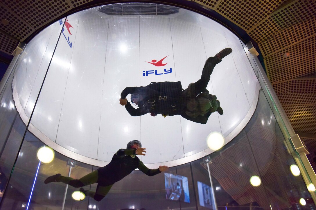 Two sailors float in a vertical wind tunnel.