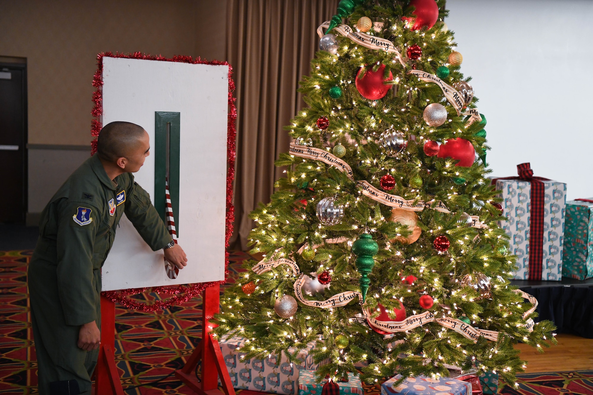 Man in military flight suit flips a switch to turn on lights on a christmas tree.
