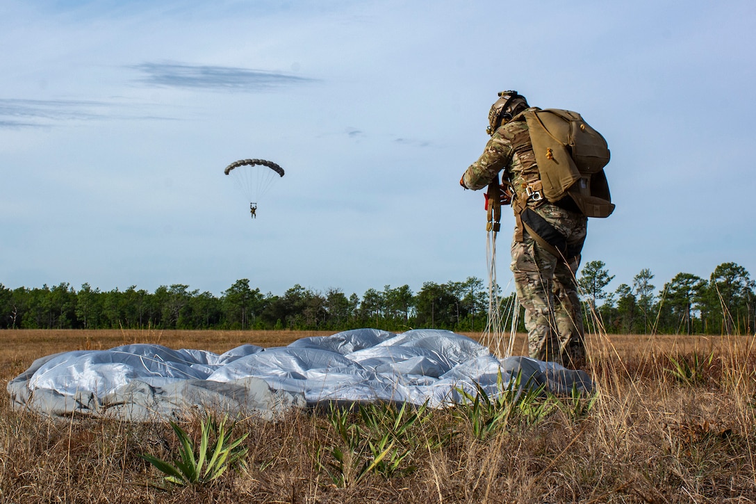 A soldier on the ground prepares to detach from a parachute as another soldier is seen coming in for a landing in the background.