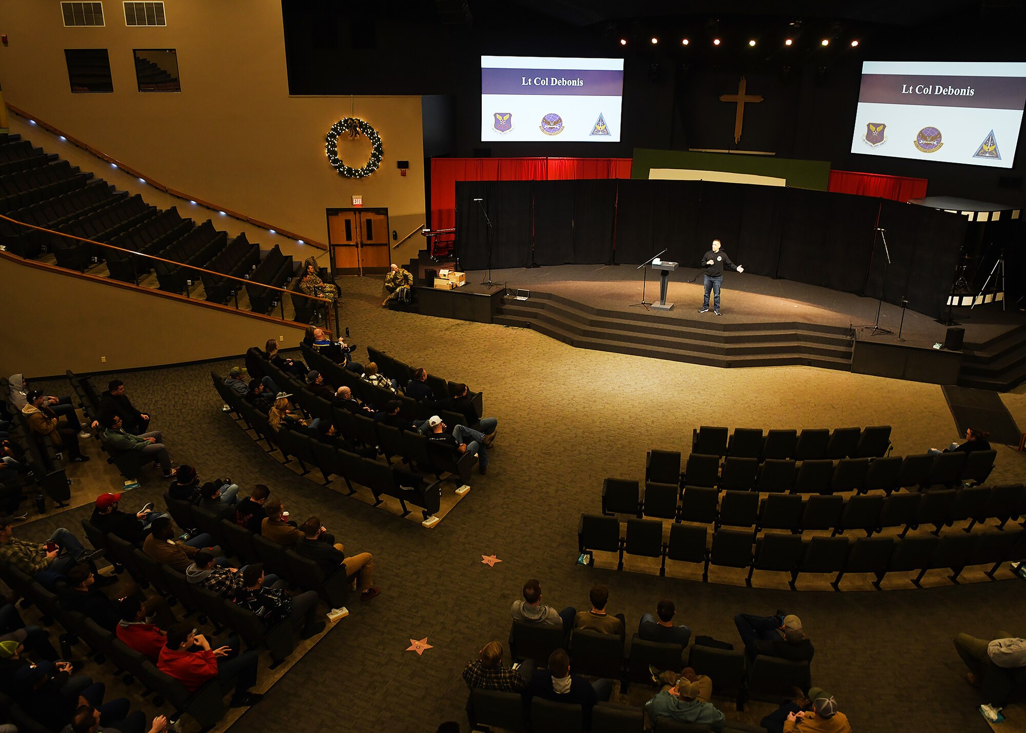 man stands on stage in a large auditorium addressing an audience.