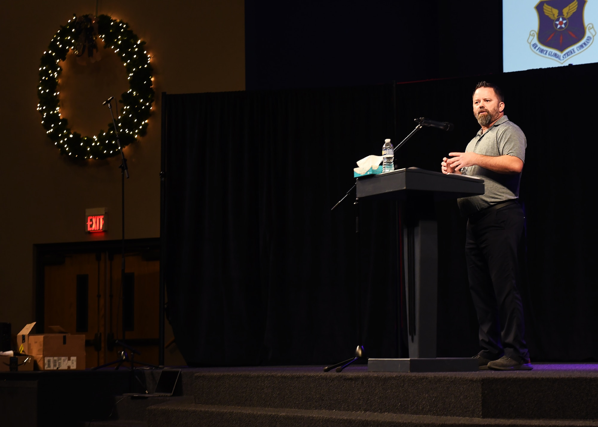 man stands on stage in front of a podium looking left.