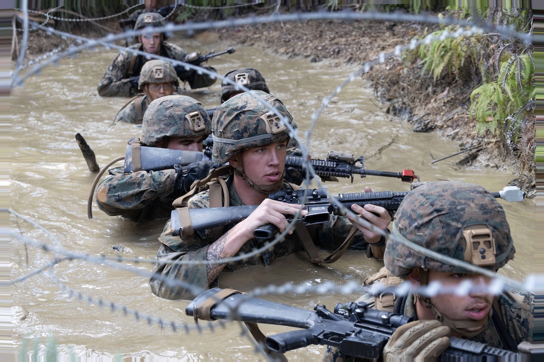 Marines creep through a muddy pool while completing the endurance portion of the Basic Jungle Skills Course at Jungle Warfare Training Center, Camp Gonsalves, Okinawa, Japan, Dec. 15, 2023. The training taught Marines to successfully navigate through dense marsh and vegetation, rappel down steep cliffs and  establish a patrol base.