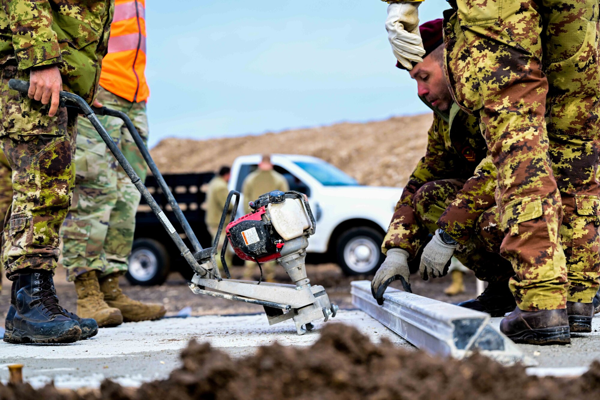 U.S. Air Force Airmen combined with Italian army personnel concrete finish part of an airfield during a training exercise.