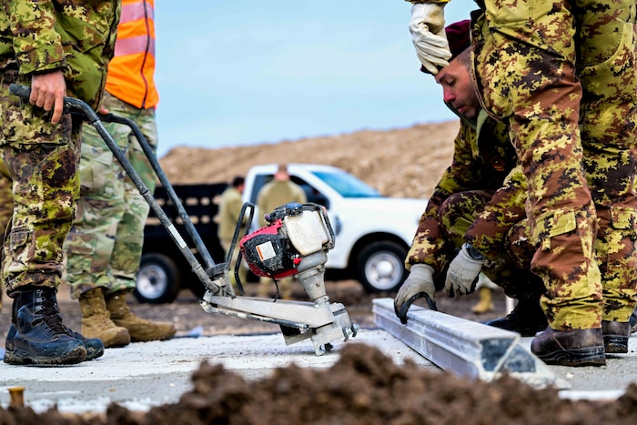 U.S. Air Force Airmen combined with Italian army personnel concrete finish part of an airfield during a training exercise.