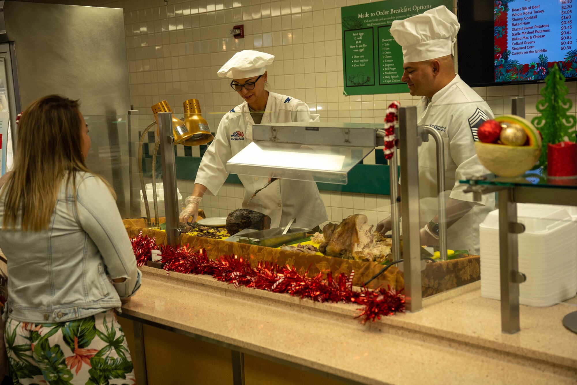 Col. Monica Gramling, 647th Air Base Group commander, and Chief Master Sgt. Gary Haley II, 647th ABG senior enlisted leader, serve Christmas Eve lunch to Airmen and families at the Hale Aina Dining Facility on Joint Base Pearl Harbor-Hickam, Hawaii, Dec. 24, 2023. The 647th Force Support Squadron hosted the lunch for several JBPHH personnel and families to ensure those who were not able to travel home during the holiday season still enjoyed a holiday meal. (U.S. Air Force photo by Senior Airman Makensie Cooper)