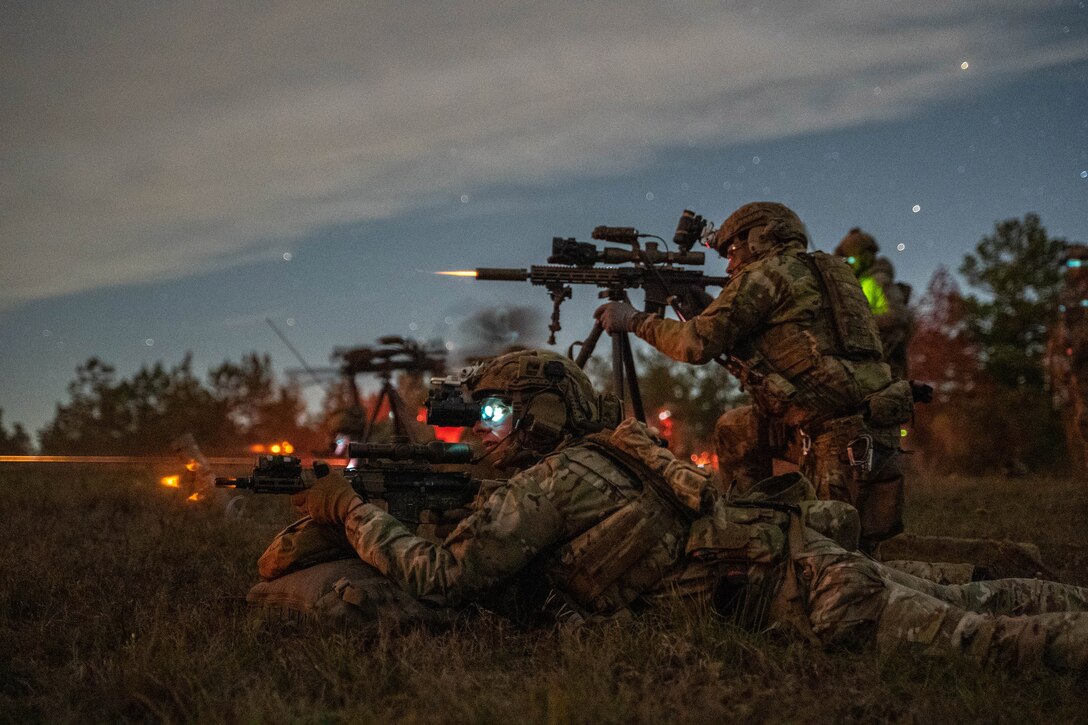 Soldiers crouching and lying prone fire weapons under a darkish, starry sky.