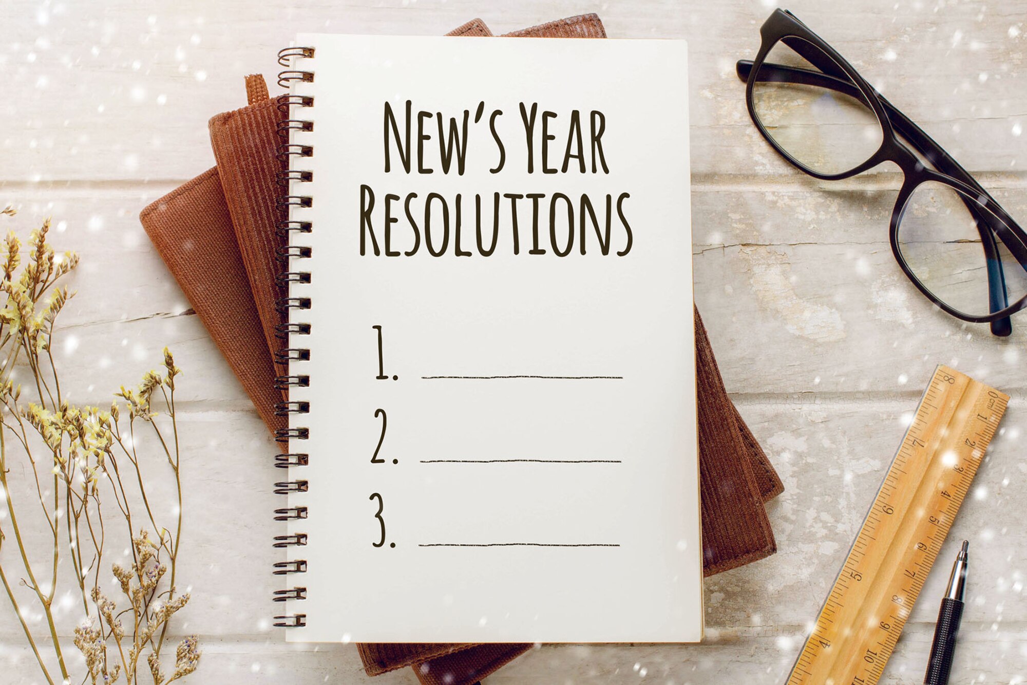 Notebook with New Year Resolutions massage, glasses and working ornament on white wooden table background.