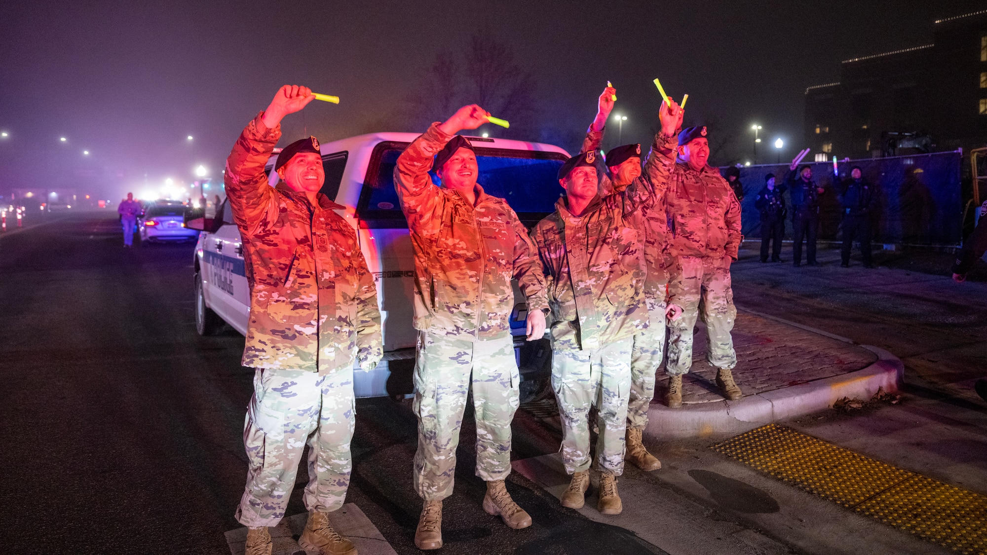 Five male United States Air Force Airmen stand in uniform waving green glowsticks.