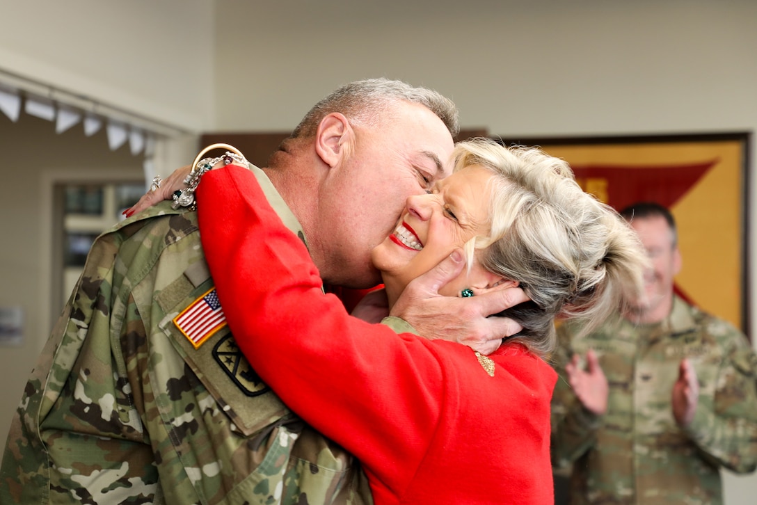 A uniformed soldier plants a kiss on the cheek of their smiling spouse.