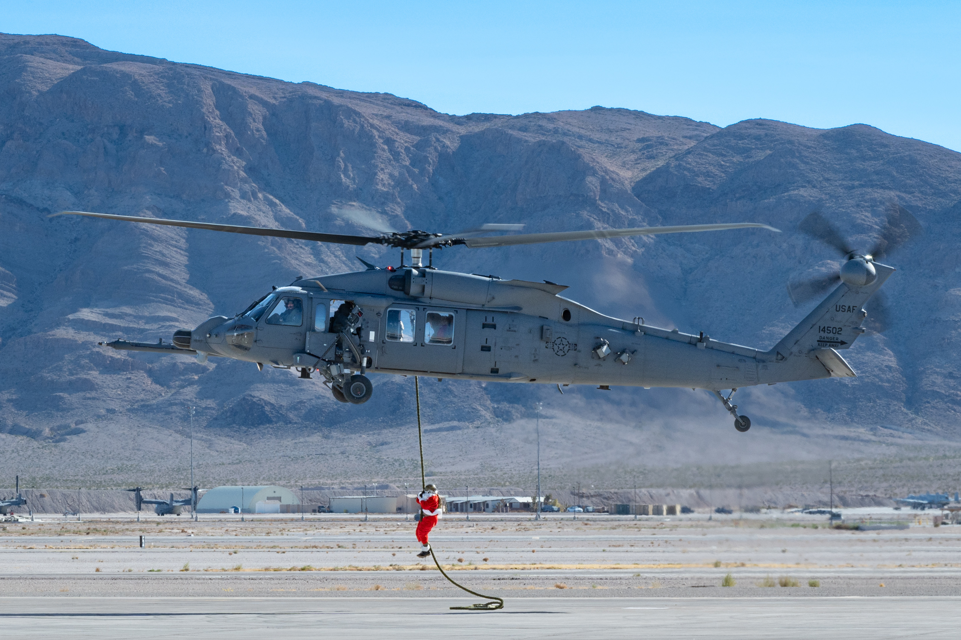 U.S. Air Force Chief Master Sgt. Jared Pietras, Senior Enlisted leader of the United States Air Force Weapons School (USAFWS), dresses up as Santa Clause and ziplines down an HH-60W at Nellis Air Force Base, Nevada, Dec. 9, 2023. This performance was dedicated to USAFWS Airmen and their families for a holiday party to build morale. (U.S. Air Force photo by Airman 1st Class Elizabeth Tan)