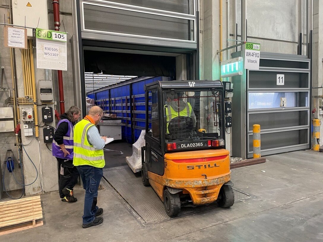 Two people standing by a forklift with driver in a warehouse.