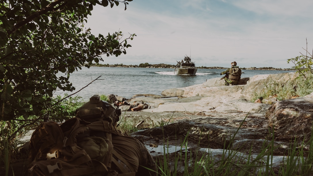 A U.S. Marine with Force Company, 2d Reconnaissance Battalion, 2d Marine Division, under tactical control of Task Force 61/2, posts security while a coastal ranger with the Swedish Marines signals to a Swedish Combat Boat 90 (CB-90) during a live-fire training evolution as a part of Exercise Archipelago Endeavor 23 in Sweden on Sept. 7, 2023. Exercise Archipelago Endeavor is an integrated, Swedish Armed Forces-led exercise that increases operational capability and enhances strategic cooperation between the U.S. Marines and Swedish forces. (U.S. Marine Corps photo by Lance Cpl. Emma Gray)