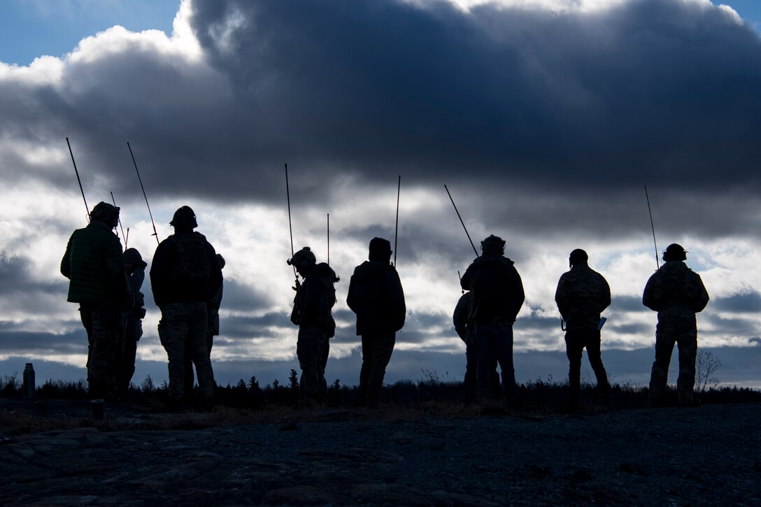 Service members stand in a group holding communication devices.