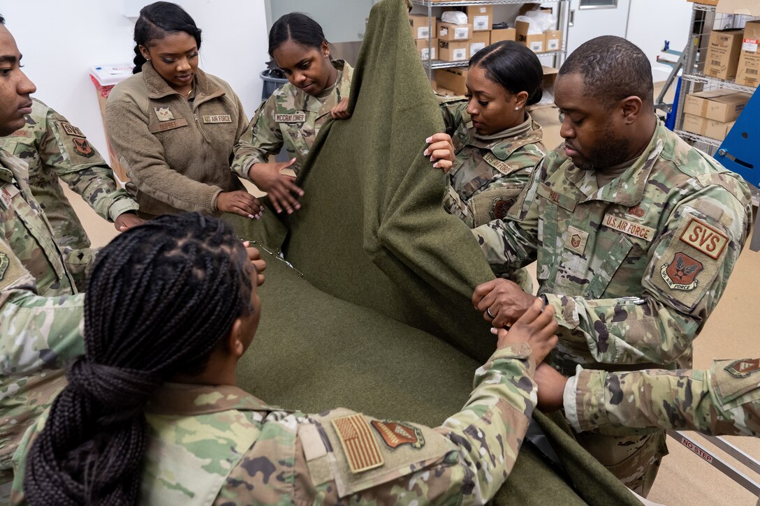 Airmen wrap a mannequin in a green blanket.