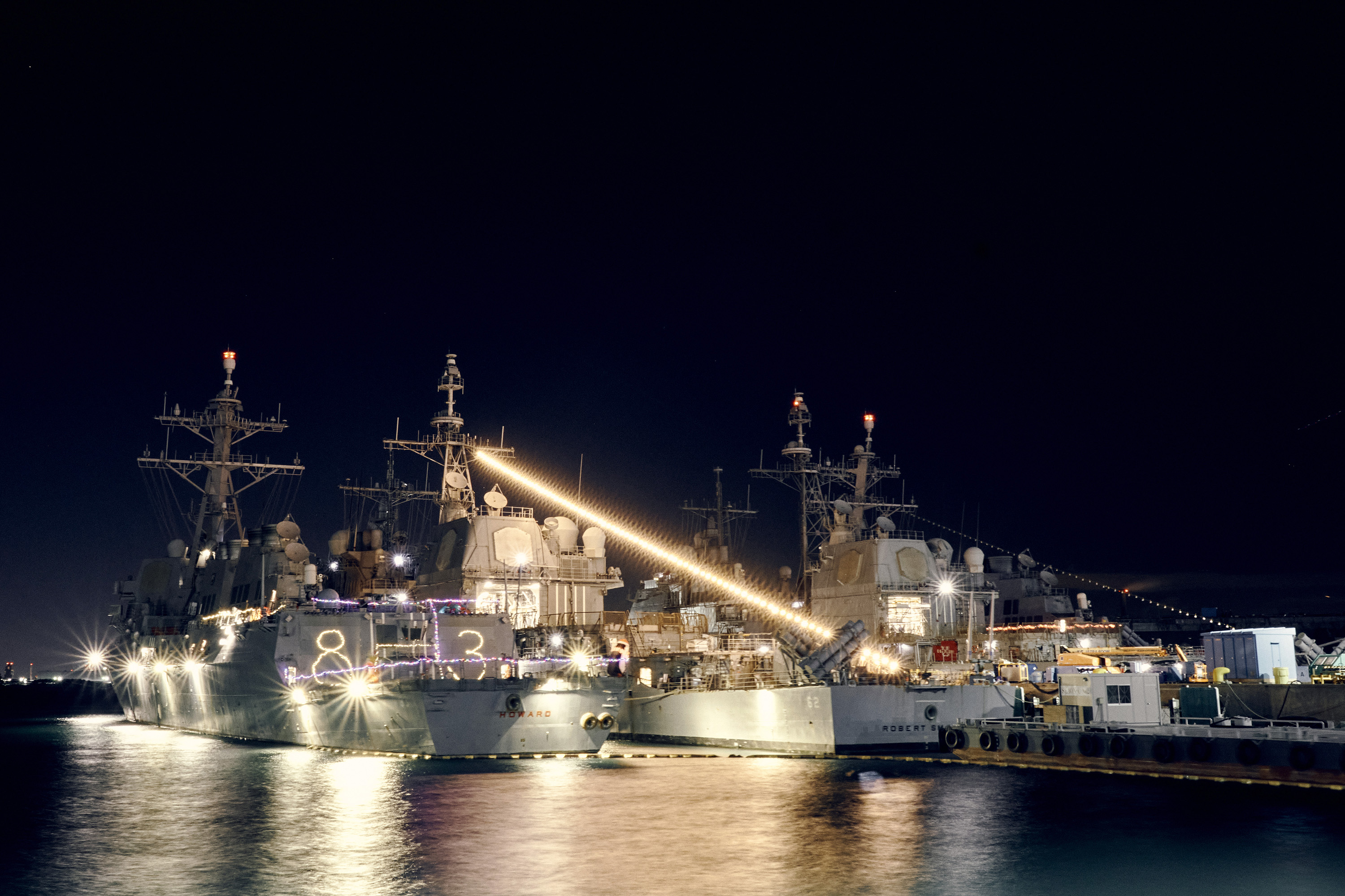 Moored ships are decorated with holiday lights, which shine against a dark sky.