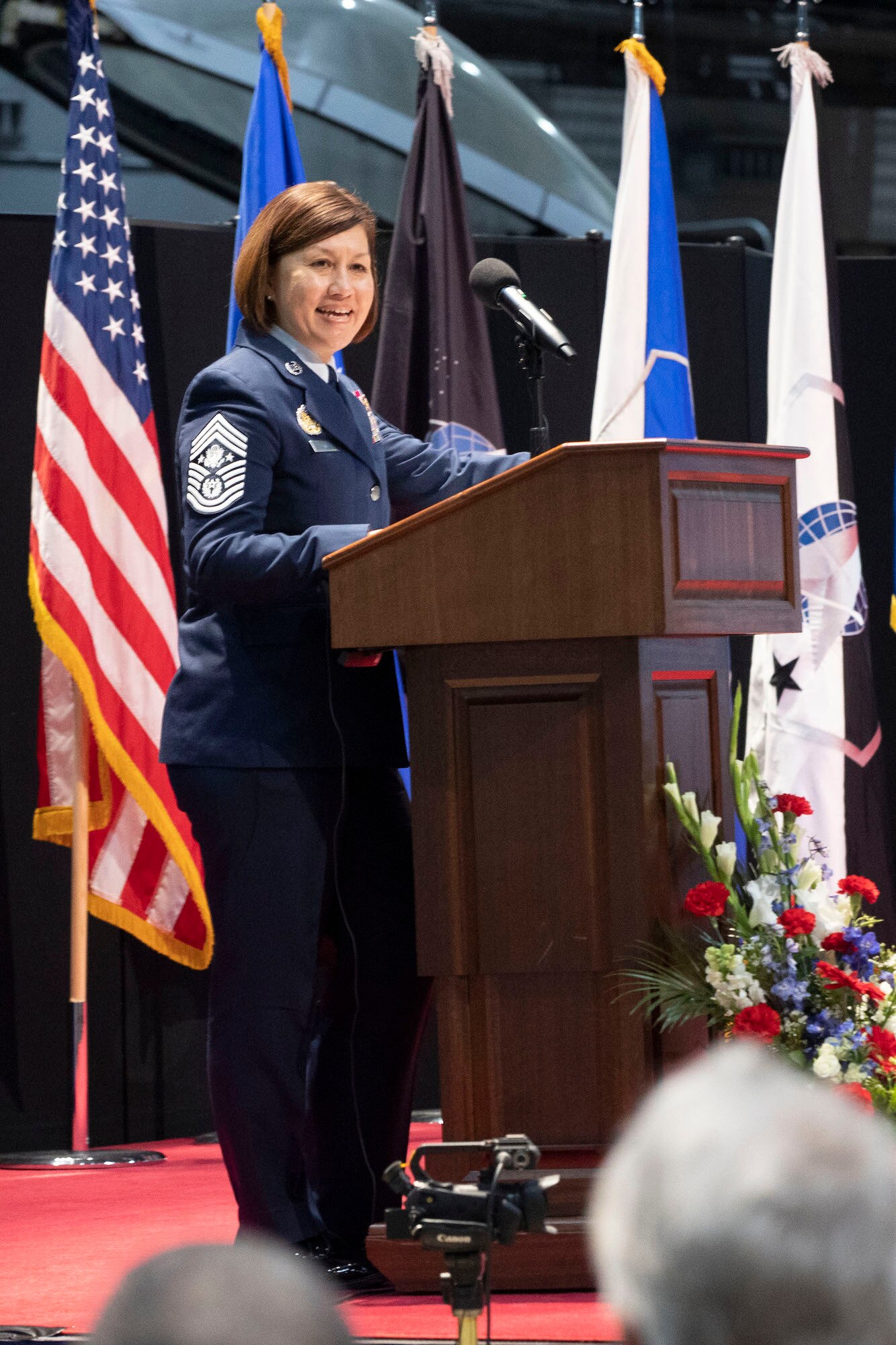 Chief Master Sergeant of the Air Force, JoAnne Bass, was keynote speaker for the opening of an Enlisted Force Exhibit at the National Museum of the U.S. Air Force on November 9, 2023. In the photo Chief Bass stands at a lectern in her blue uniform.