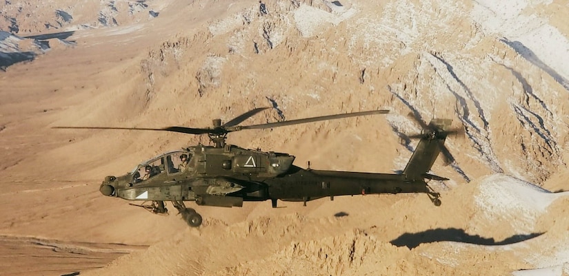 An Army helicopter flies over barren, hilly terrain.