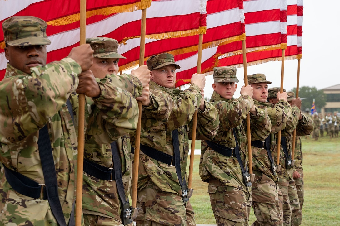 Seven airmen hold flags in formation during an outdoor ceremony on an overcast day.