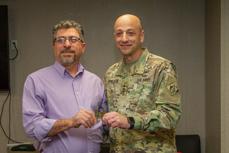 A man in a purple button up shirt receives a coin from a man in a military uniform.