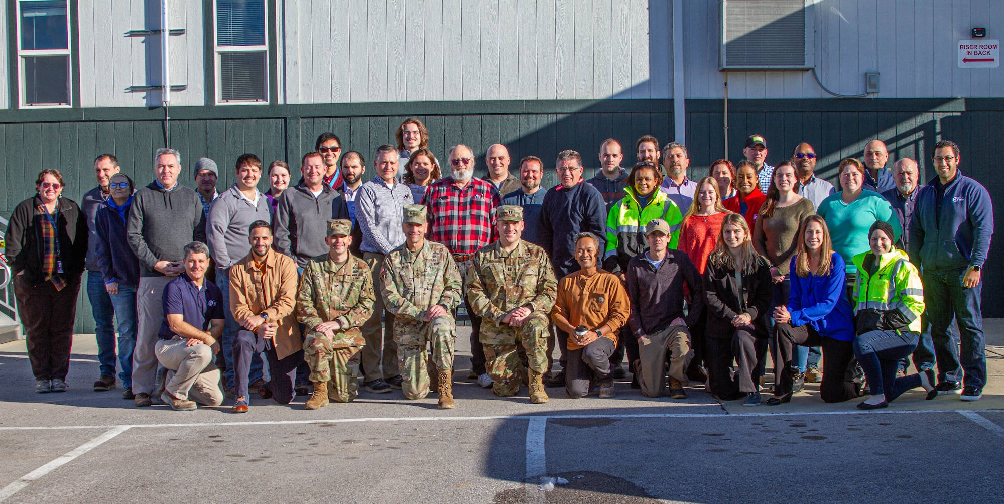 Many people are lined up for a group photo outside a construction trailer.