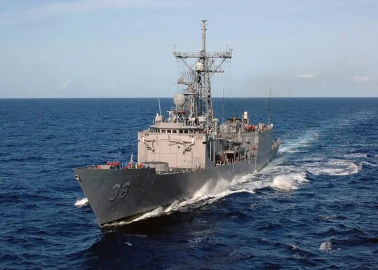 A Navy ship underway on a dark blue sea with a light blue sky