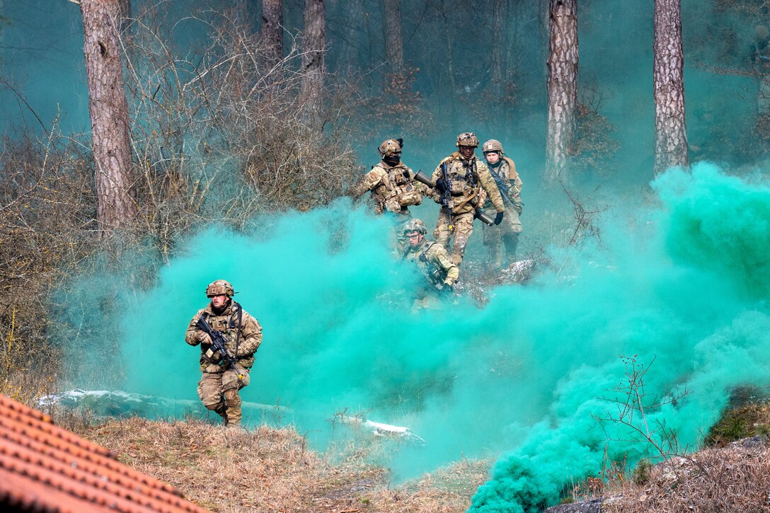 Soldiers run down a hill through a haze of green smoke during an exercise.